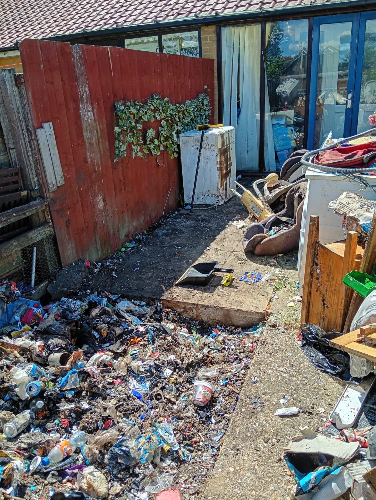 A back courtyard carpeted with scattered household litter in front of a red gate
